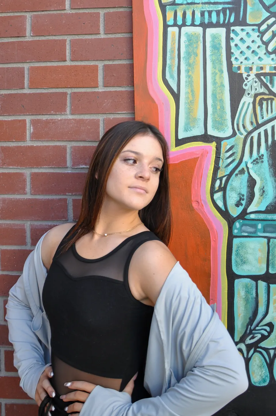 Dancer in a mesh-panel leotard and grey hoodie against a brick wall and mural