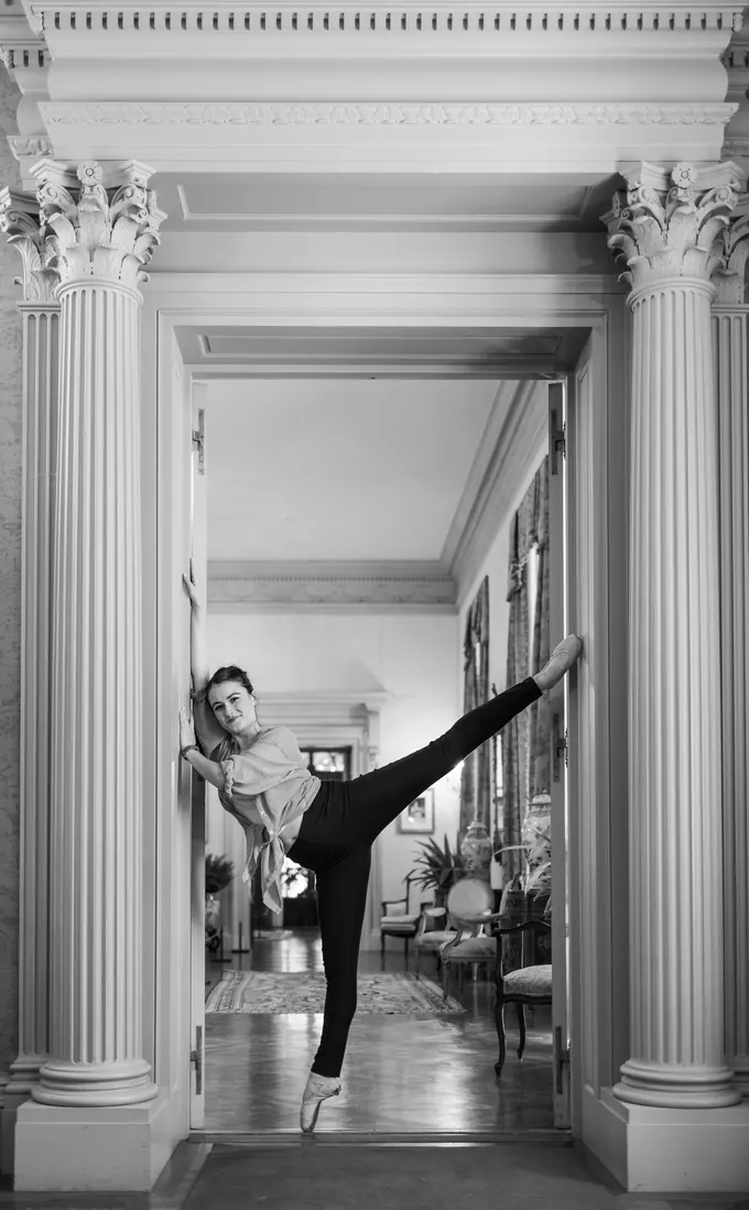Black and white photo of a dancer in an arabesque framed by a columned doorway